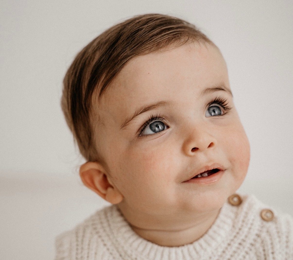 Baby met blauwe ogen in gebreid vestje kijkt lachend omhoog